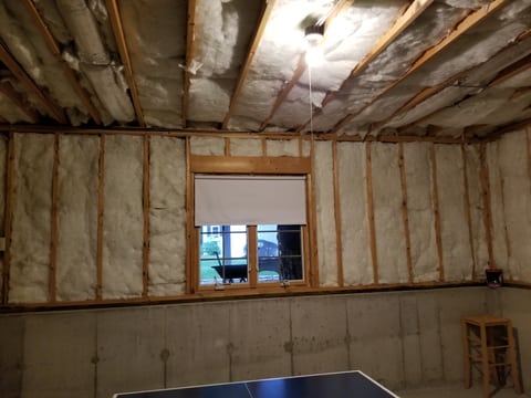 Unfinished basement wall and ceiling with exposed wood framing, insulation, a window, and a concrete lower wall.