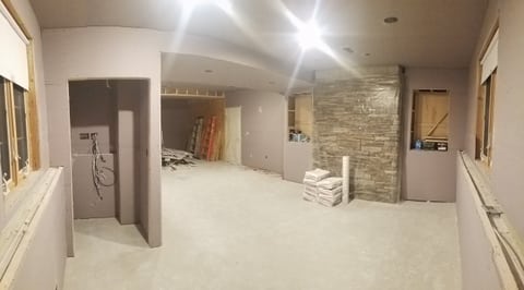 A wide basement view with wallboard on the walls and ceiling, unfinished joints, and open trim areas.