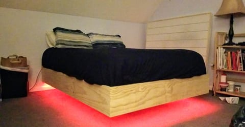 A wood-sided platform bed and white headboard with red light illuminating the floor beneath the recessed base.