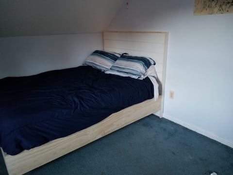 A platform bed with visible wood grain on the side, dark bedding, and a white paneled headboard.