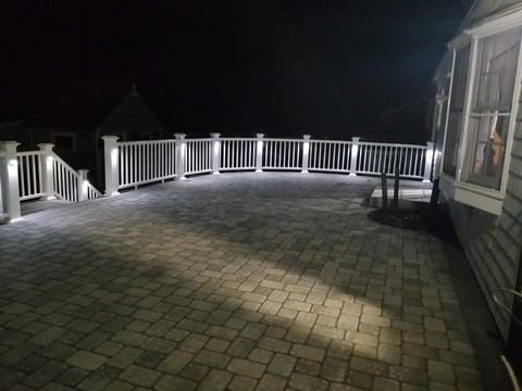 The paved patio at night with small lights illuminating the white railing and the edge of the paving.