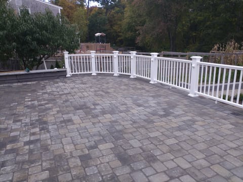 A broad patio paved with rectangular blocks in varied gray and tan tones, bordered by white railing.